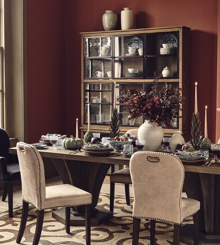 A dining room scene featuring a long wooden, rectangular dining table, leather dining chairs and tableware.