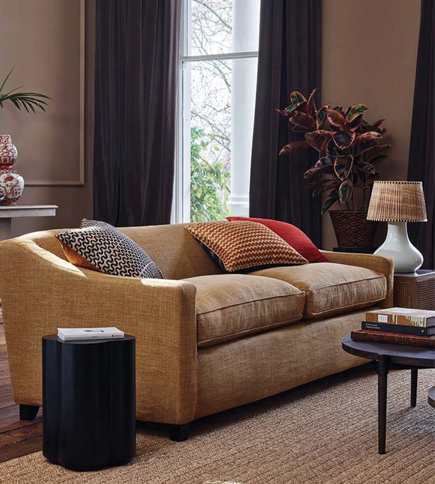 A lounge with a yellow sofa, a coffee table and a lamp in-front of a large window with floor length curtains.