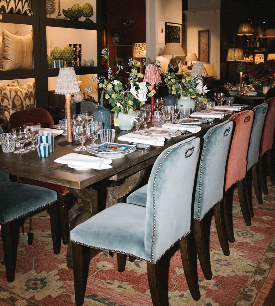 A row of blue and red velvet dining chairs arranged around a rectangular dining table, with the table set with patterned accessories and flowers.