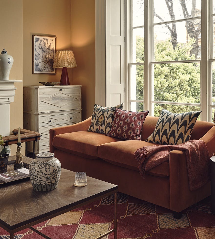 A cozy fall sitting room featuring an orange velvet sofa decorated with patterned pillows.