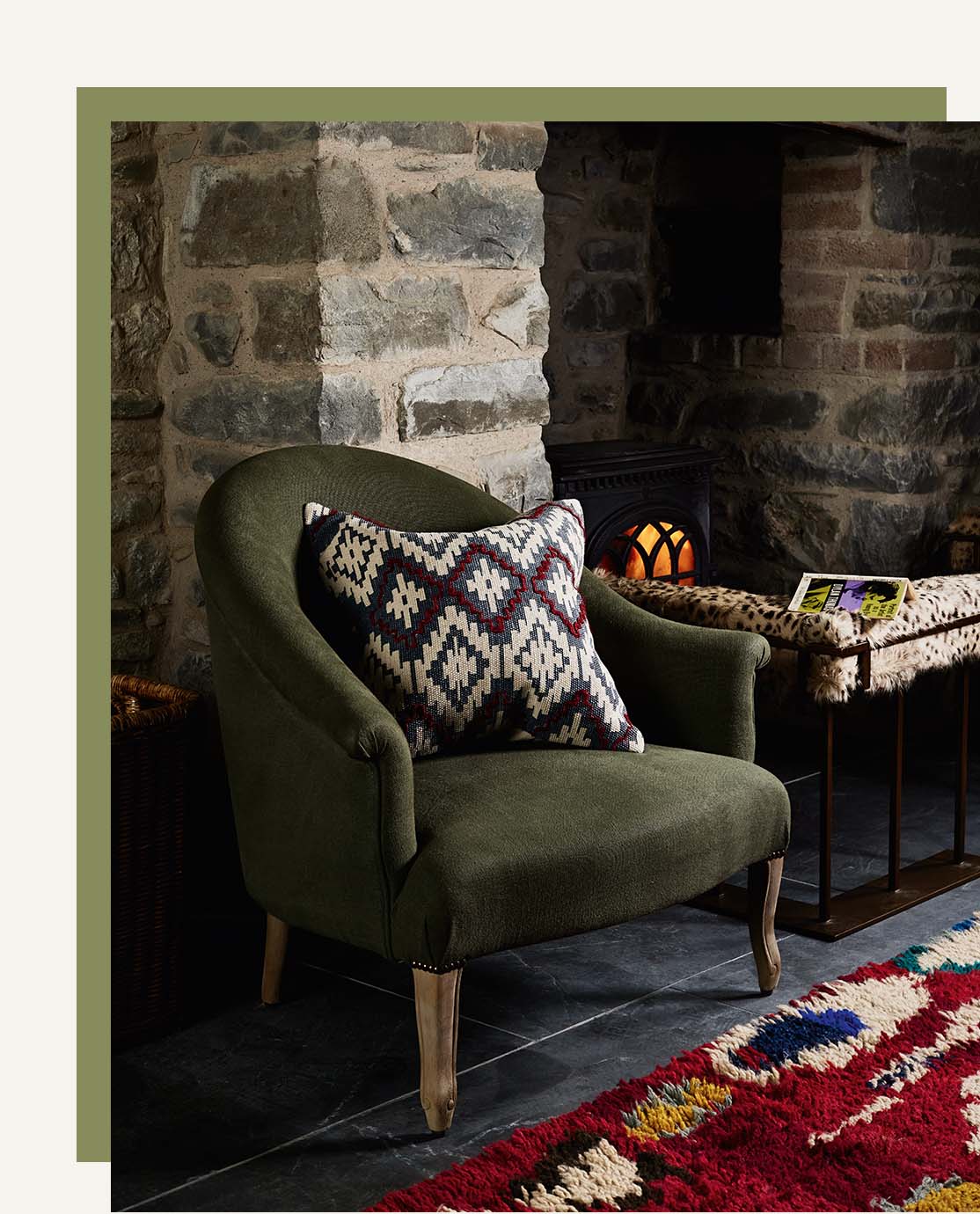 A green armchair next to a cheetah fire fender and a lit fireplace