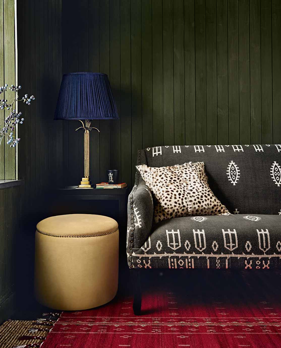 A cosy cottage setting, featuring a printed sofa, yellow ottoman and a navy blue and gold lamp