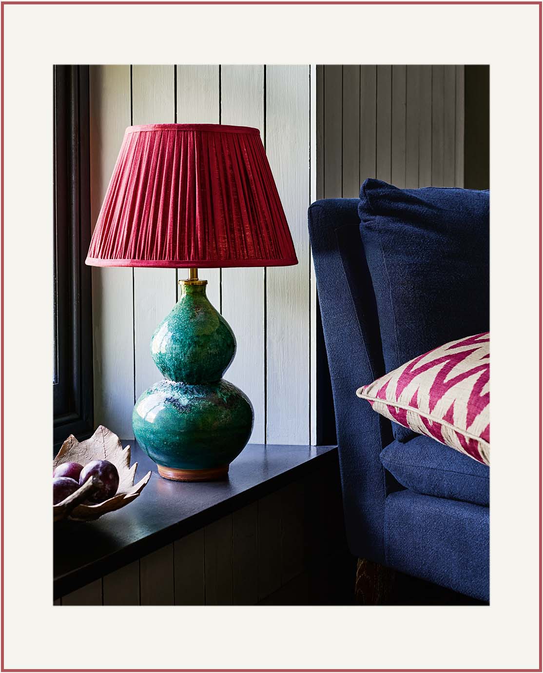 A aquamarine table lamp decorated with a pleated red lampshade