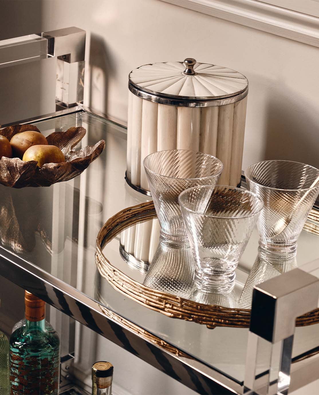 White bone ice bucket and glassware sit on a mirroed bar cart