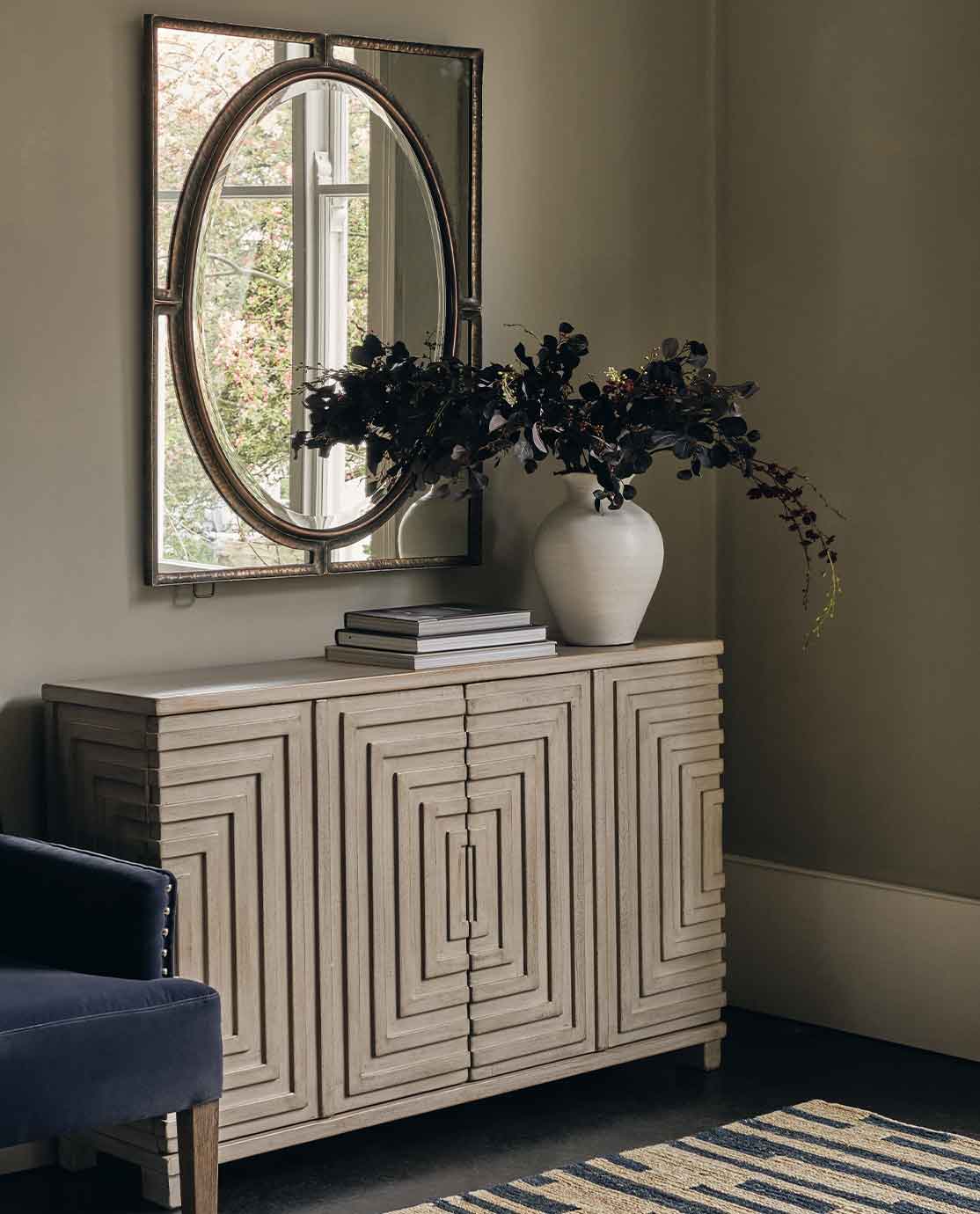 A console table featuring a stack of books and a plant, in front of a rustic mirror