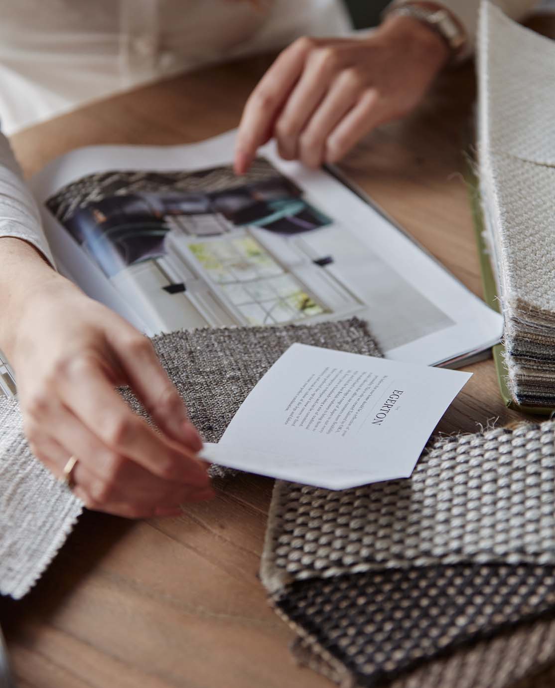 A close-up of a woman's hands as she looks through the OKA magazine. There are fabric swatches on the table.