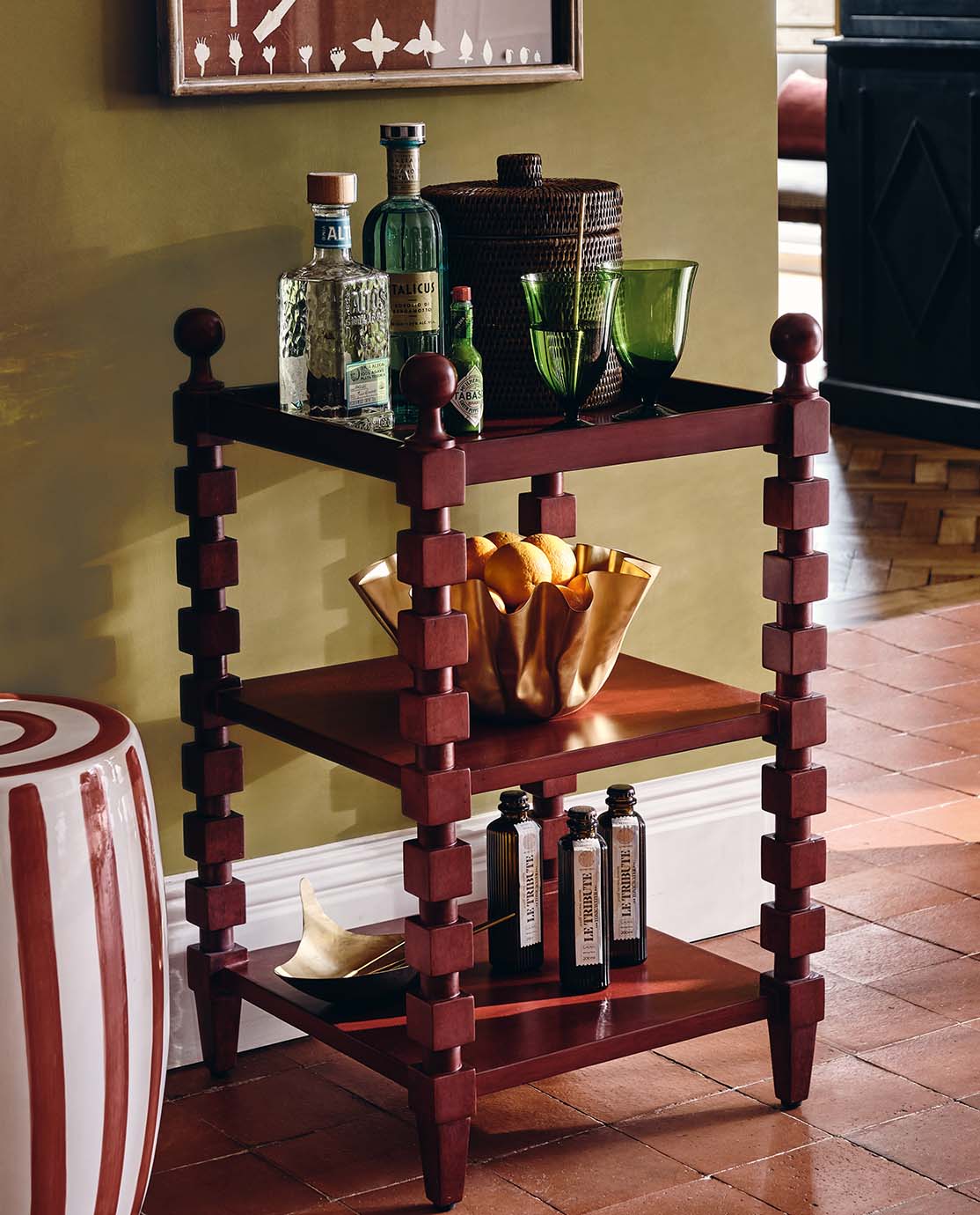 A red side table with cubed, bobbin-style legs, holding a selection of drinks and colorful glassware.