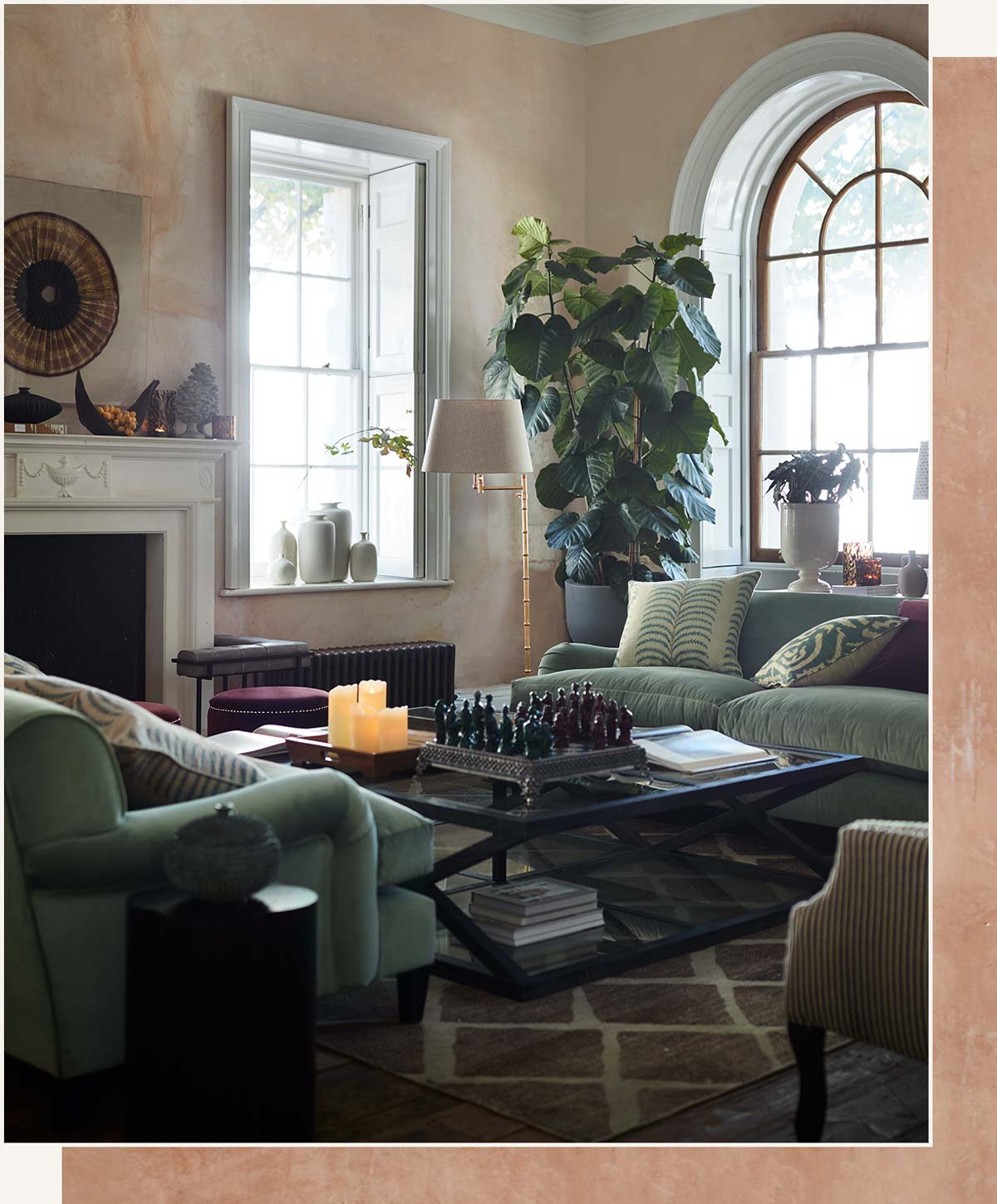 A sitting room setting, with light blue sofas, a black and glass coffee table and a brown rug. The walls are plastered and there is a large arched window in the background.