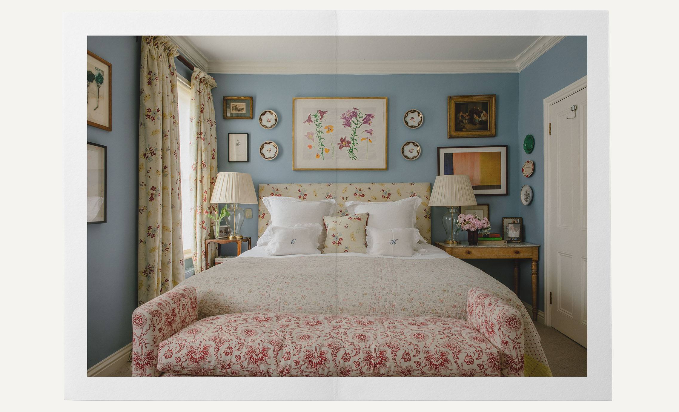 A blue bedroom with a floral ottoman, floral headboard and floral bedding