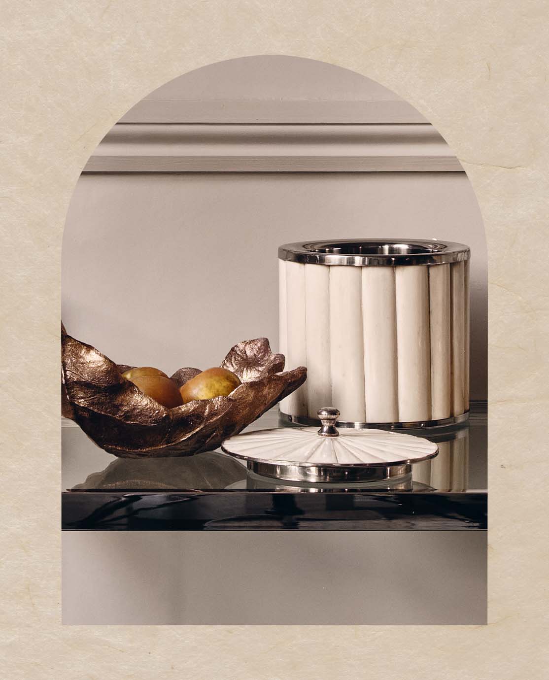 A white bone ice bucket and decorative leaf dish sit on a mirrored bar cart