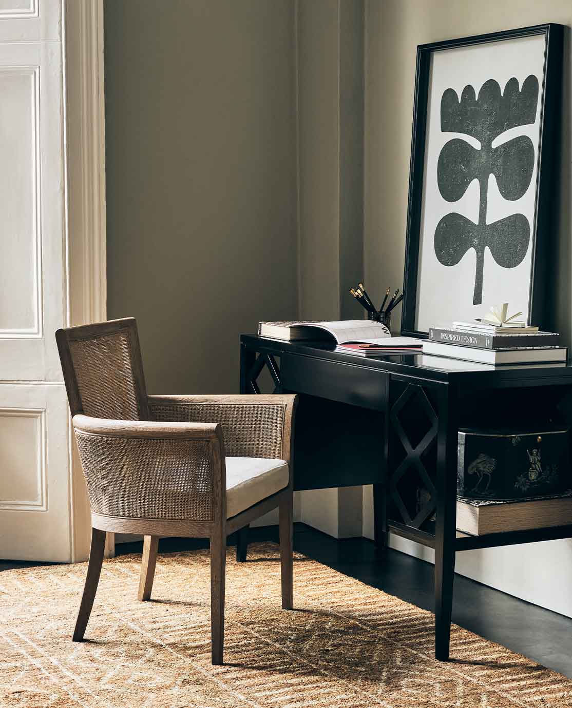 A rattan armchair in front of a black desk, decorated with a monochrome abstract print