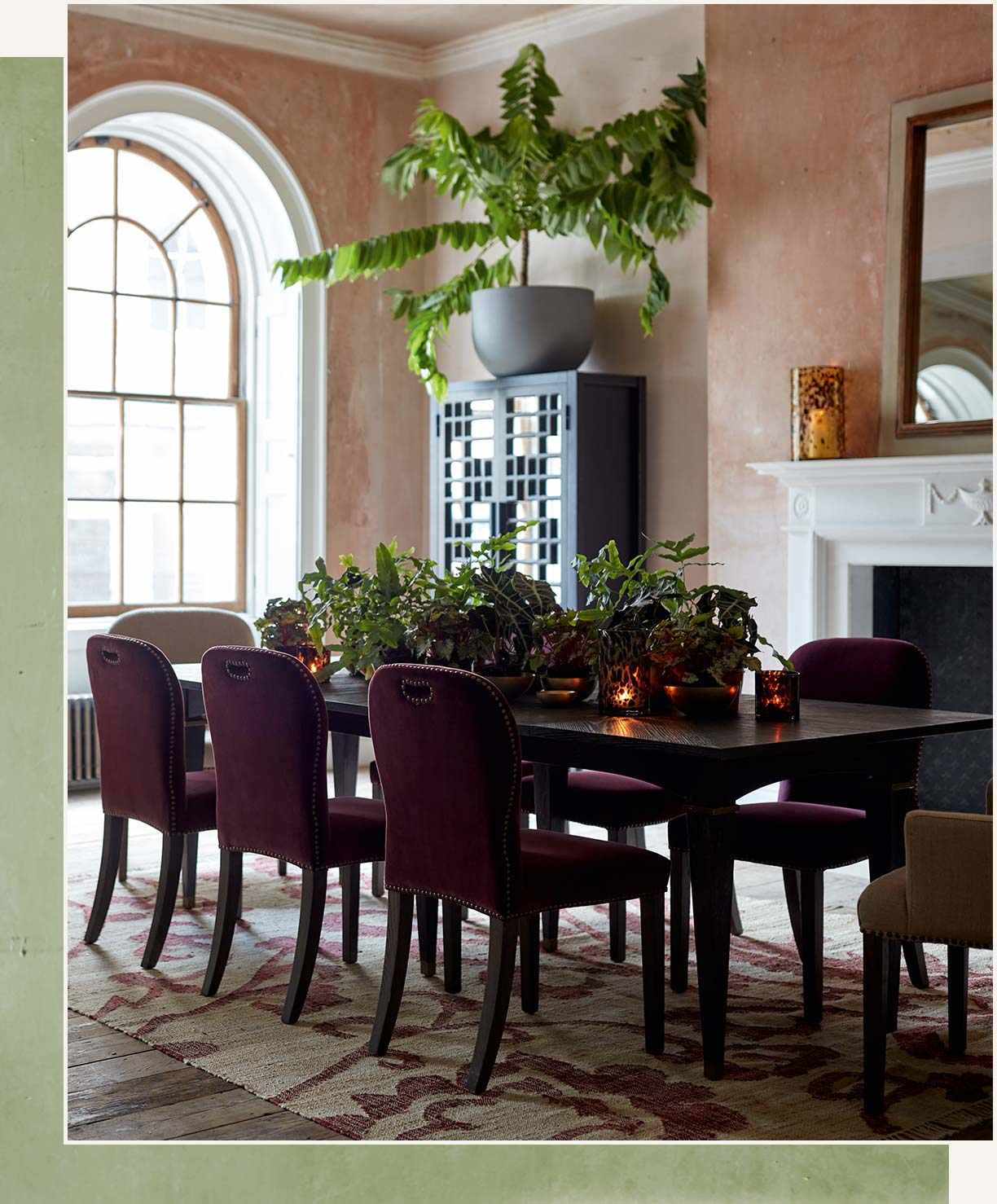 A large black dining table and red velvet chairs sit on top of a patterned rug in a heritage building.