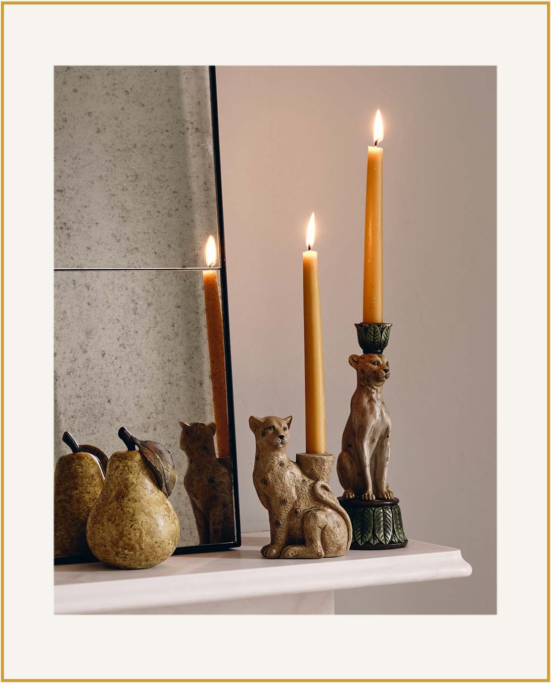 Two leopard candle holders sit on a white mantelpiece next to a decorative pear