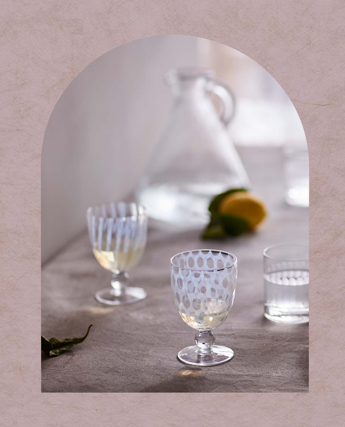 Two patterned wine glasses sit in front of a glass jug