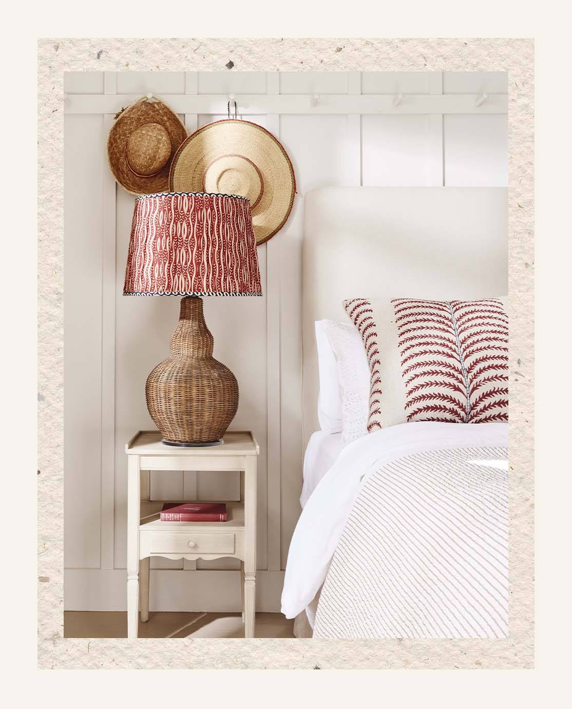 A rattan lamp base, topped with a red and blue printed lampshade, sits on a white wooden nightstand.