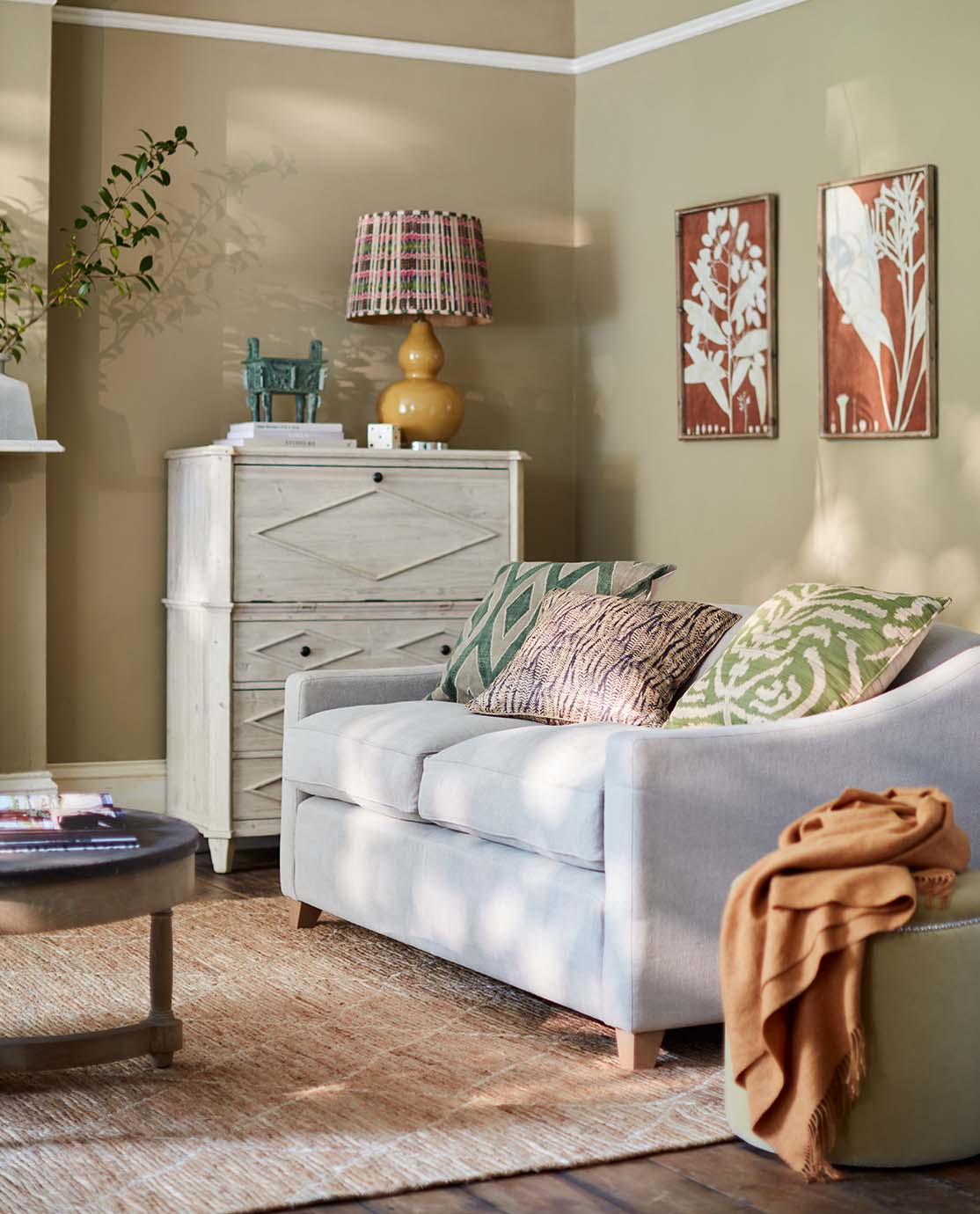 A colourful sitting room setting, with a light blue loveseat decorated with printed cushions. 