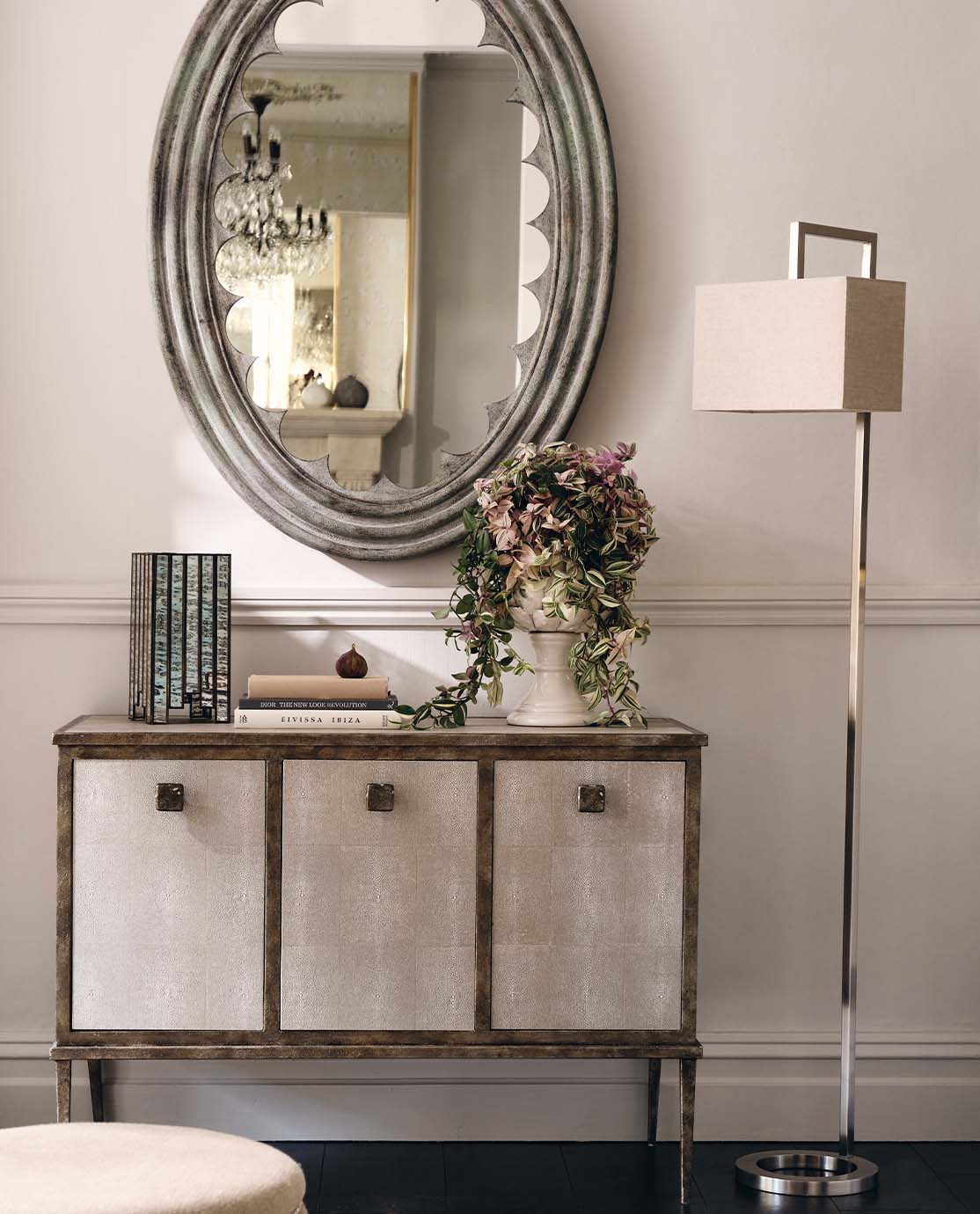 A faux shagreen console table stands next to a silver floor lamp and elegant mirror