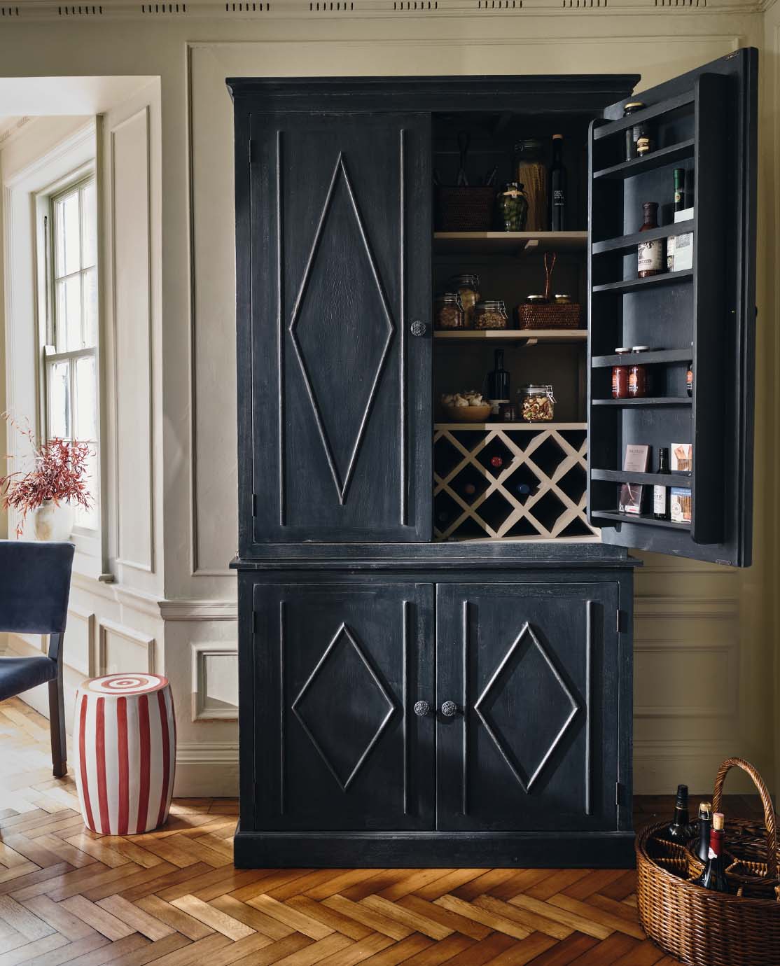 A large indigo pantry cabinet, decorated with diamond detailing. One door is open, revealing a jars of condiments and glassware.