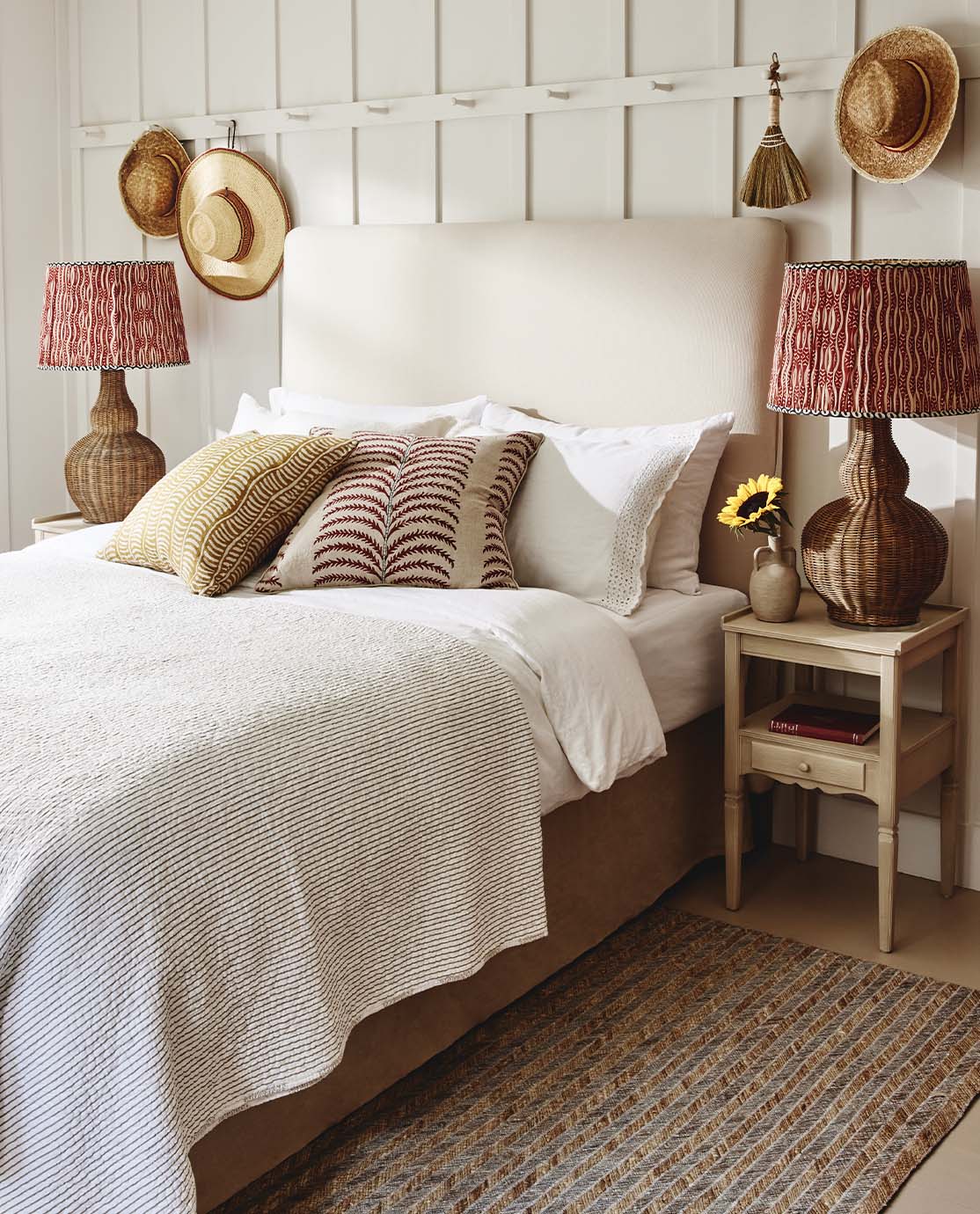 A rattan lamp, topped with a red, white and blue printed lampshade, sits on a white wooden nightstand. 