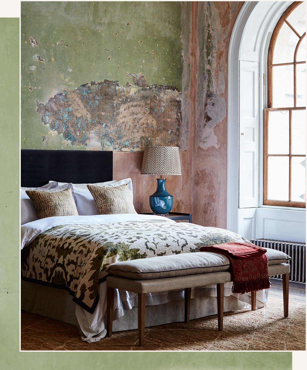 A bedroom setting with distressed walls, a bed with a patterned throw and an upholstered bench.