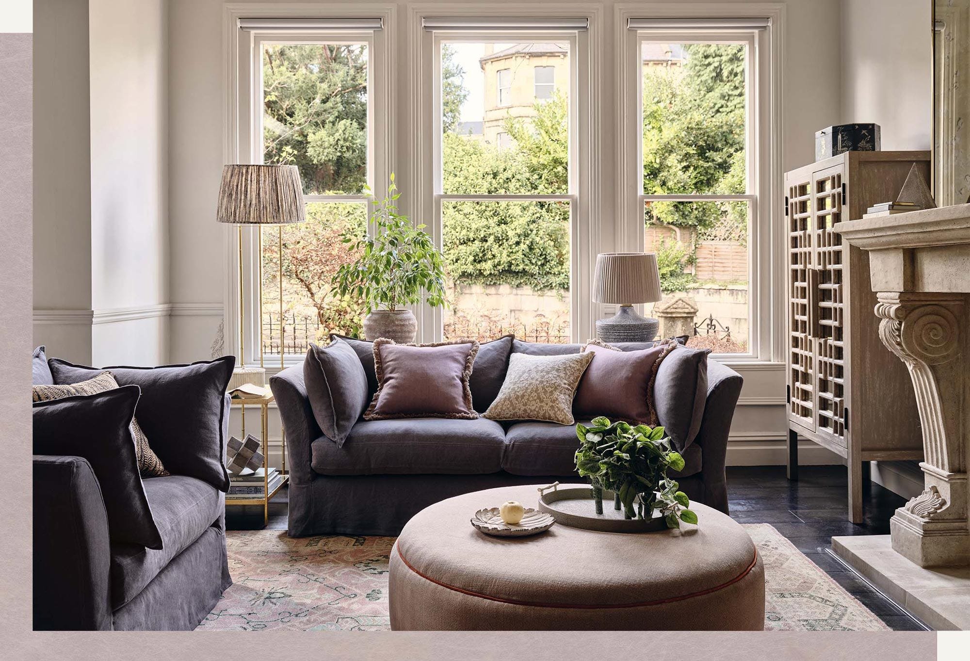 A sitting room setting with navy sofas, a round, grey ottoman and printed pillows