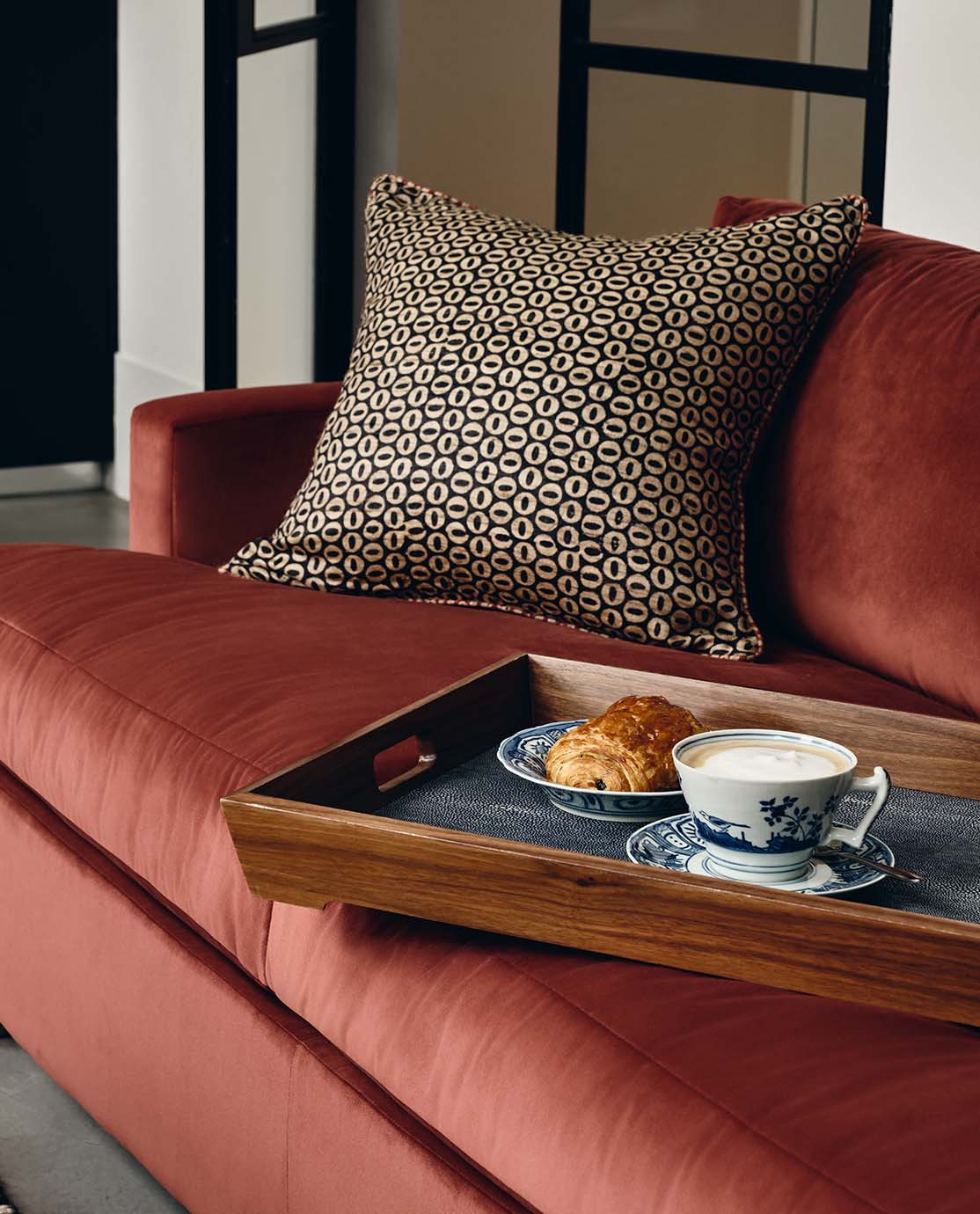 A blood orange Clever Velvet sofa. A breakfast tray holding a croissant and a cup of tea are balanced on it.