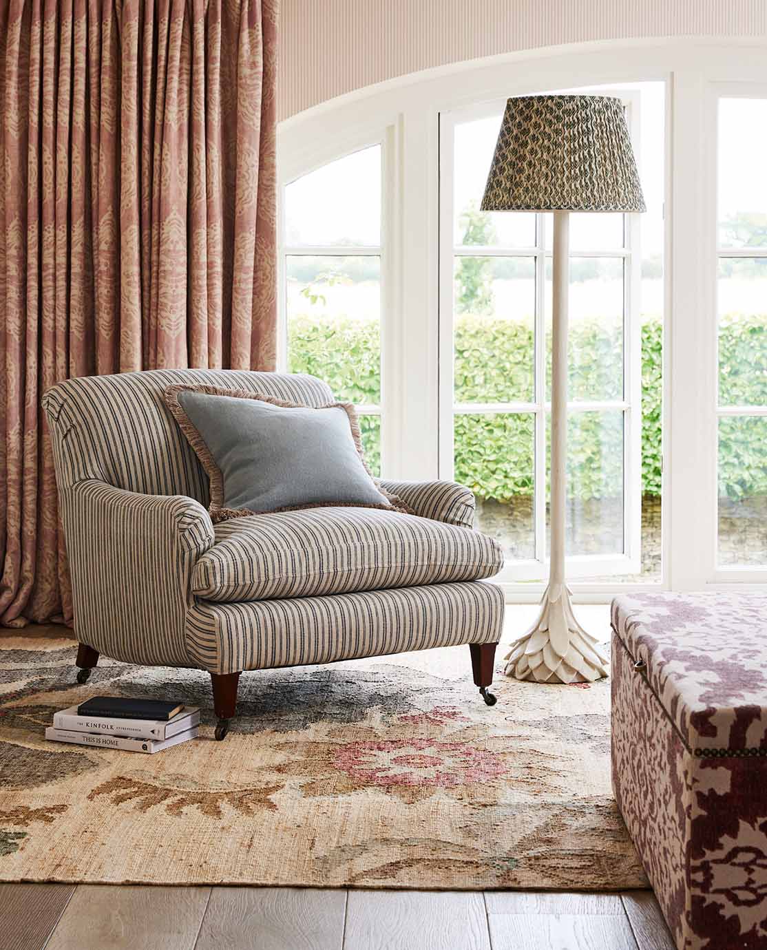 A striped armchair, decorated with a blue fringed pillow, sits on a patterned rug next to a white floor lamp.