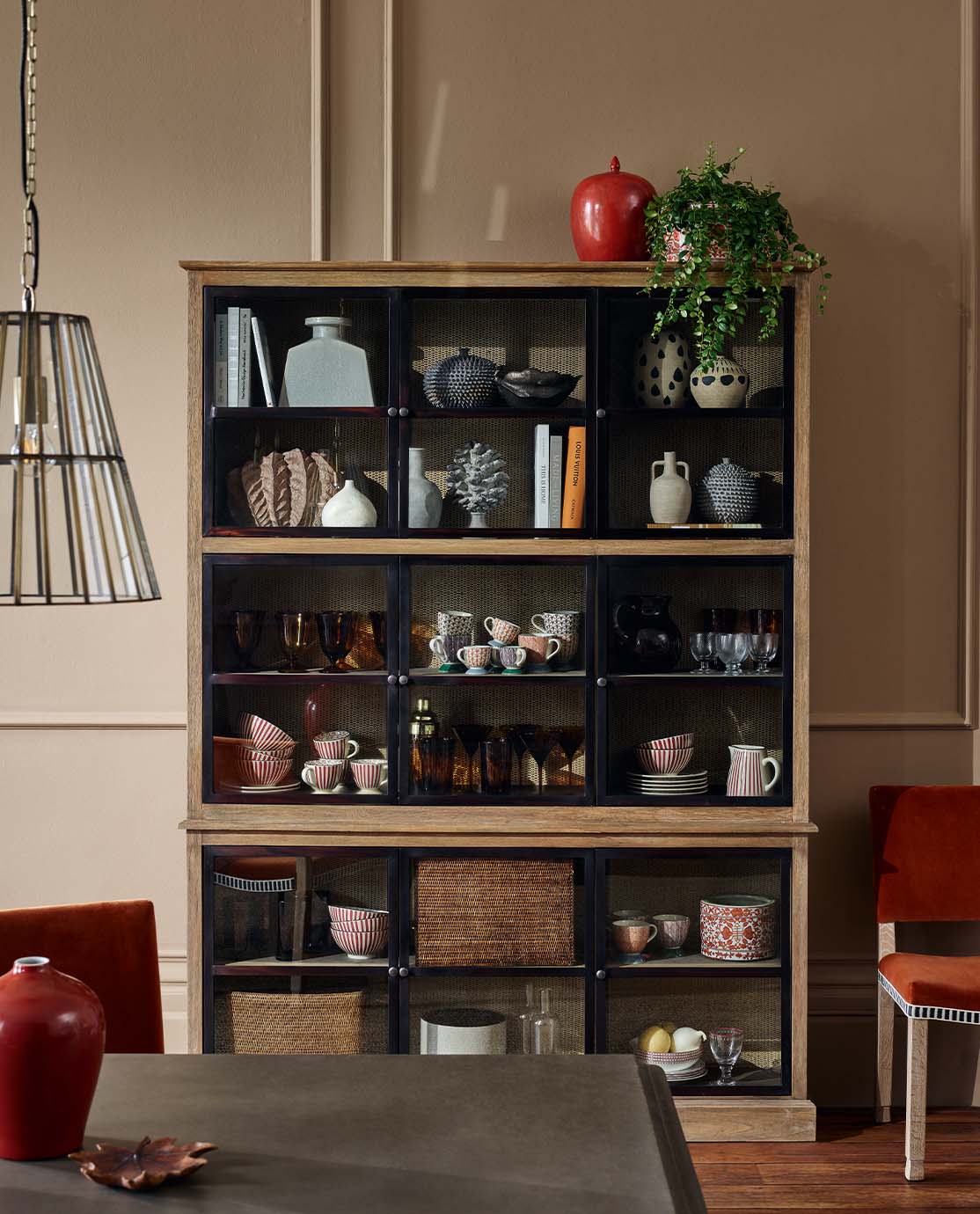 A large glass-fronted display cabinet in a dining room, dressed with printed vases, ornaments and dinnerware.