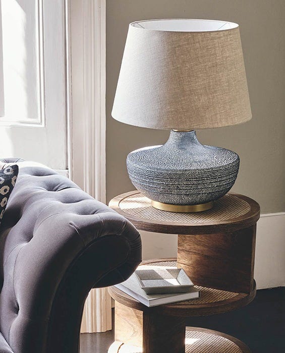Velvet sofa flanked by a wooden side table with a lamp on it