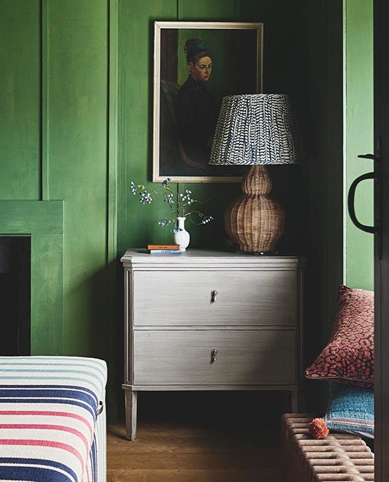 A green room with a small grey chest of drawers, topped with a rattan lamp