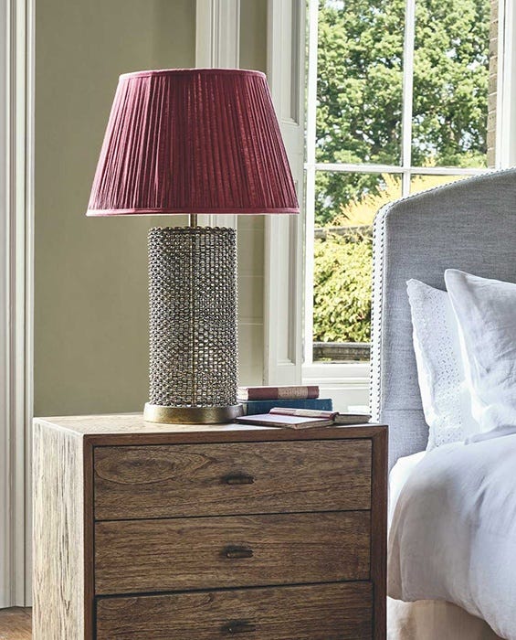 Next to a bed, there's a small wooden bedside table with a metal lamp on top