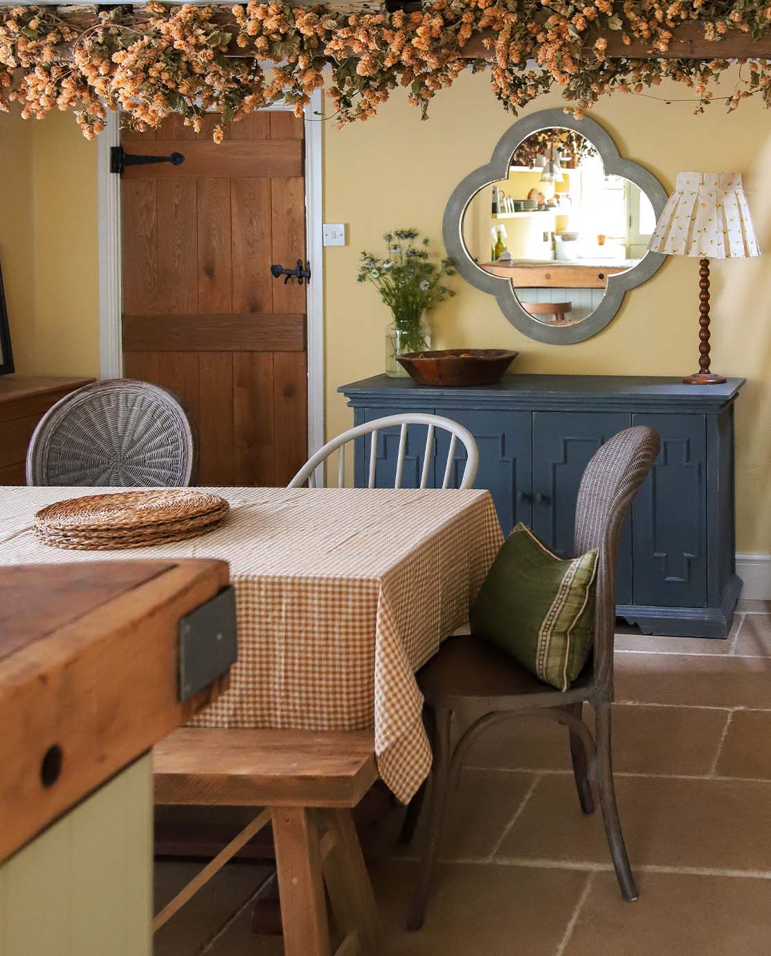 A kitchen with butter yellow walls, a blue sideboard and a table covered with a red-and-white gingham tablecloth.