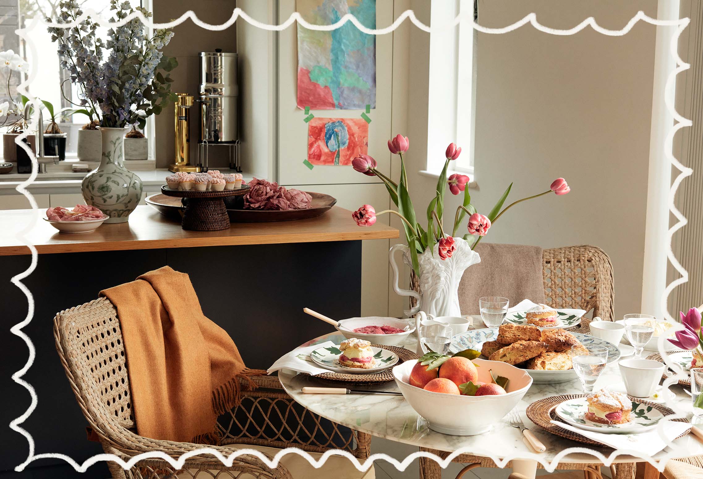 A rattan chair is pulled up to a marble dining table, which is set with crockery, tulips and baked goods