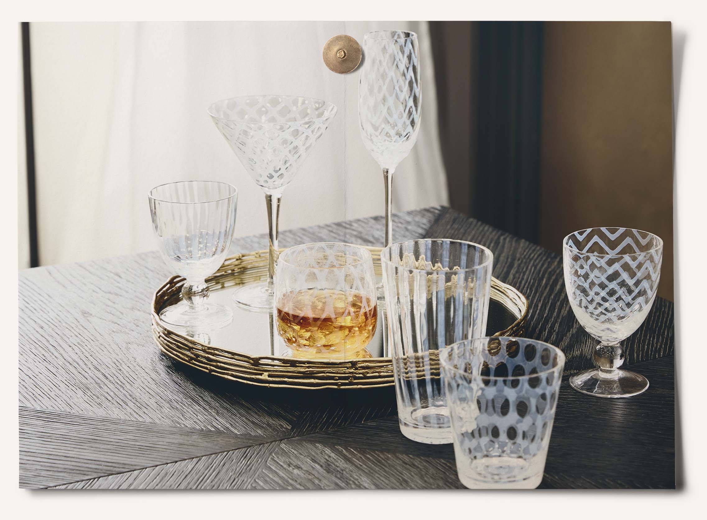 A selection of OKA's Pulcinella glassware, featuring striped, zigzag and polka dot prints, arranged on a mirrored brass tray.