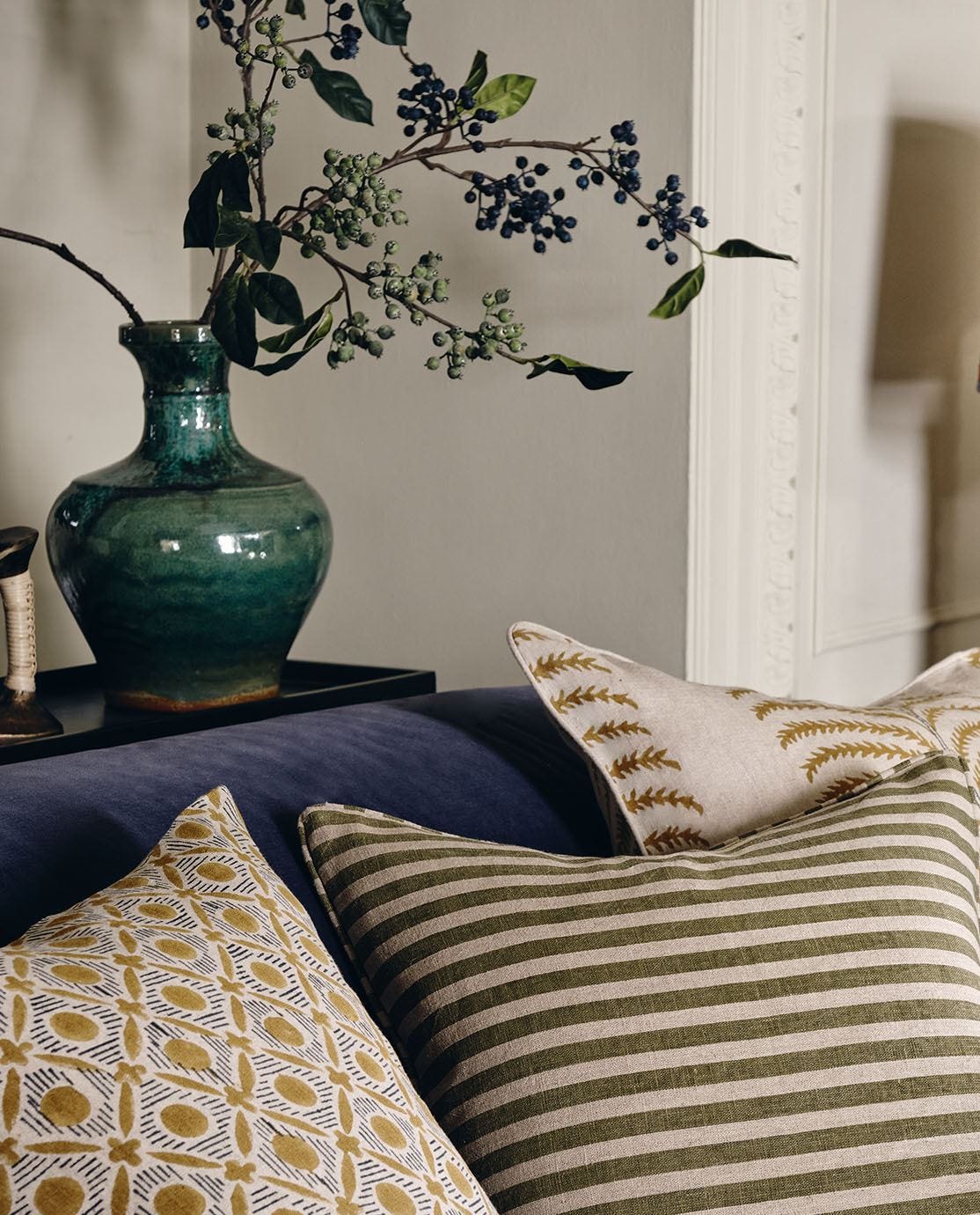 A green vase sits on a console table behind a velvet sofa, decorated with patterned cushions.