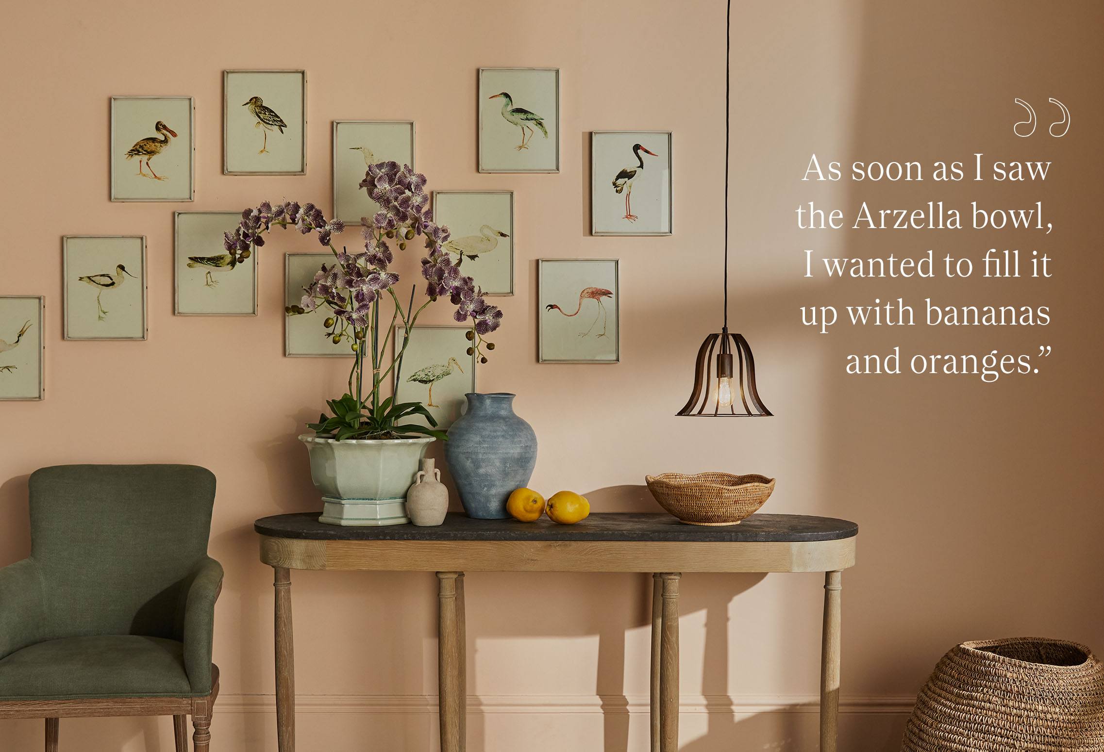 A console table decorated with accessories, leaning against a pale pink wall which is decorated with framed prints of birds.