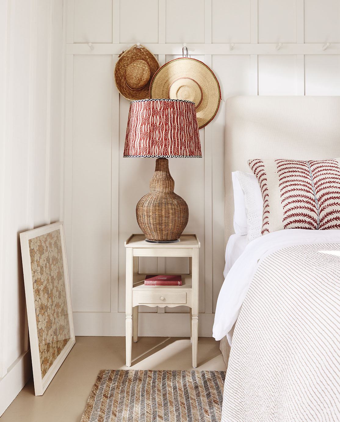 A wooden chest of drawers is decorated with a sculptural leaf lamp, a vase of faux leaves and a tray of beauty products.