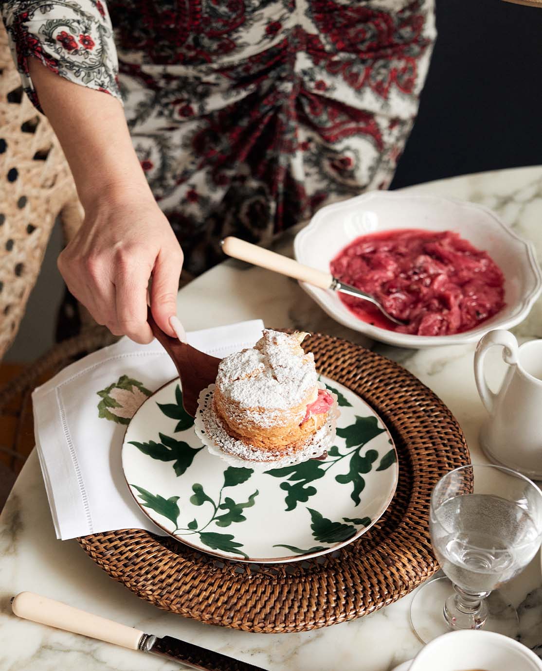 Claire serves a scone on a white china plate decorated with a green leaf pattern