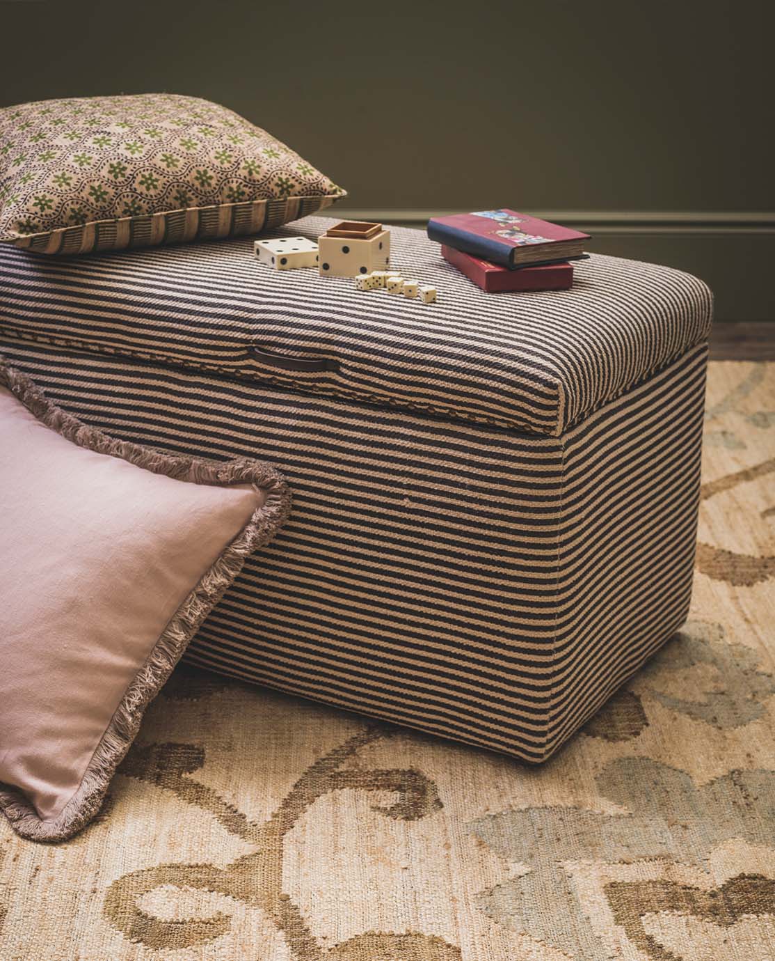 A striped fabric ottoman decorated with patterned cushions and games.