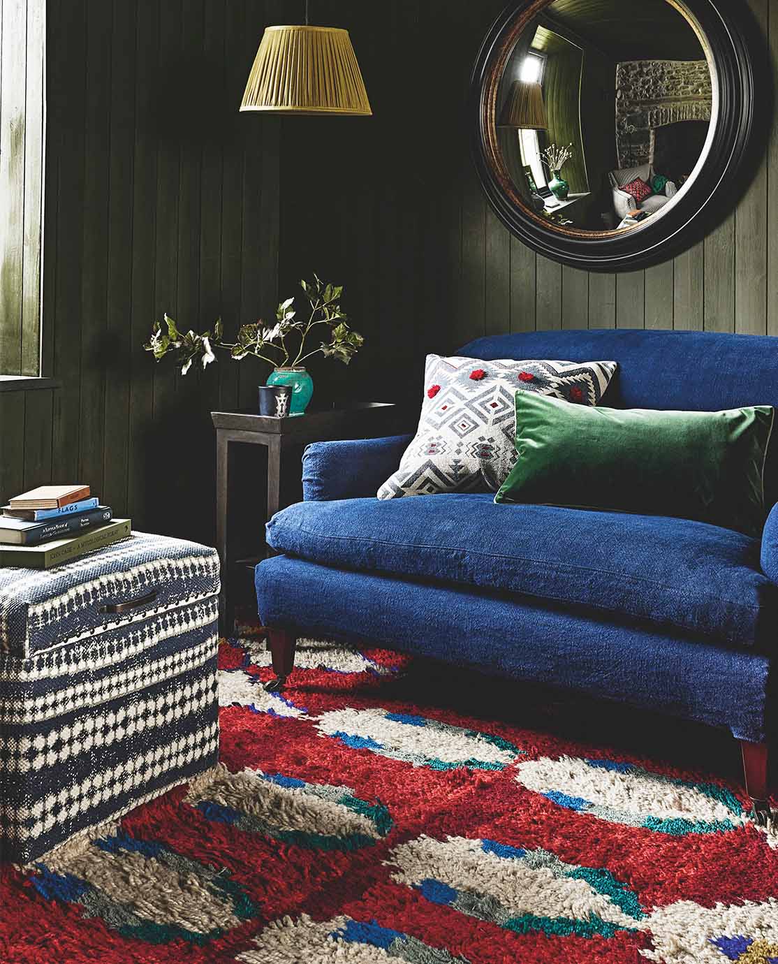 A sitting room setting with a navy blue sofa, a red patterned rug and a trunk ottoman with printed blue upholstery