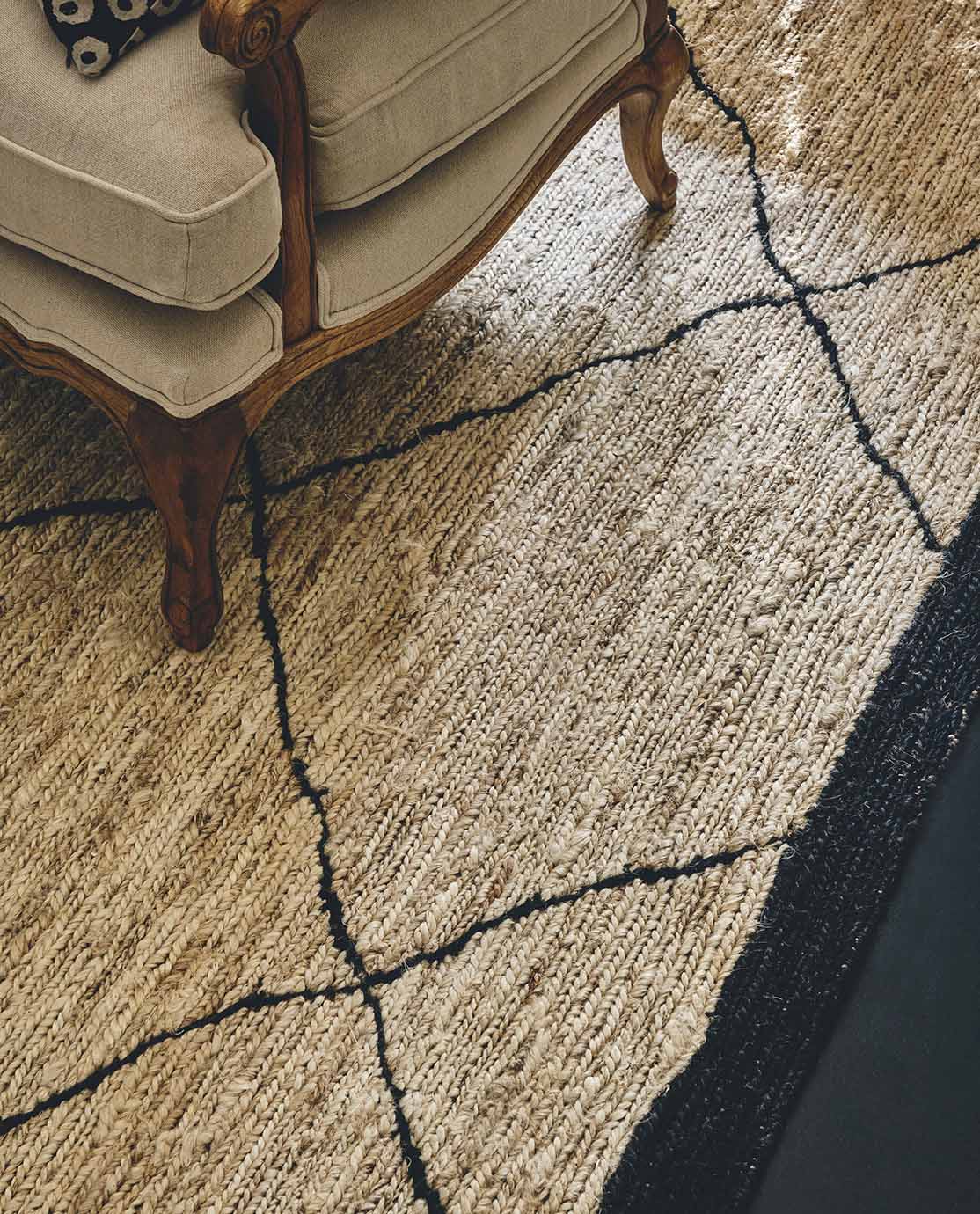 A wooden and cream-upholstered armchair resting on a jute rug