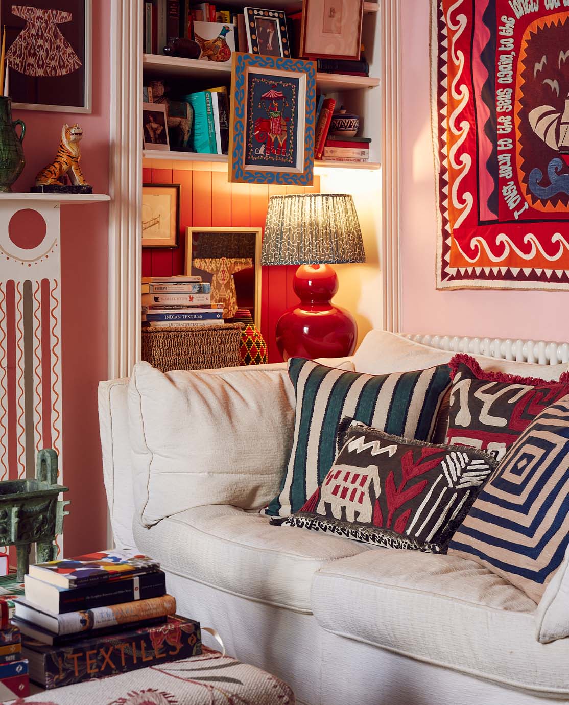 A white sofa covered with colourful cushions, in a pink room