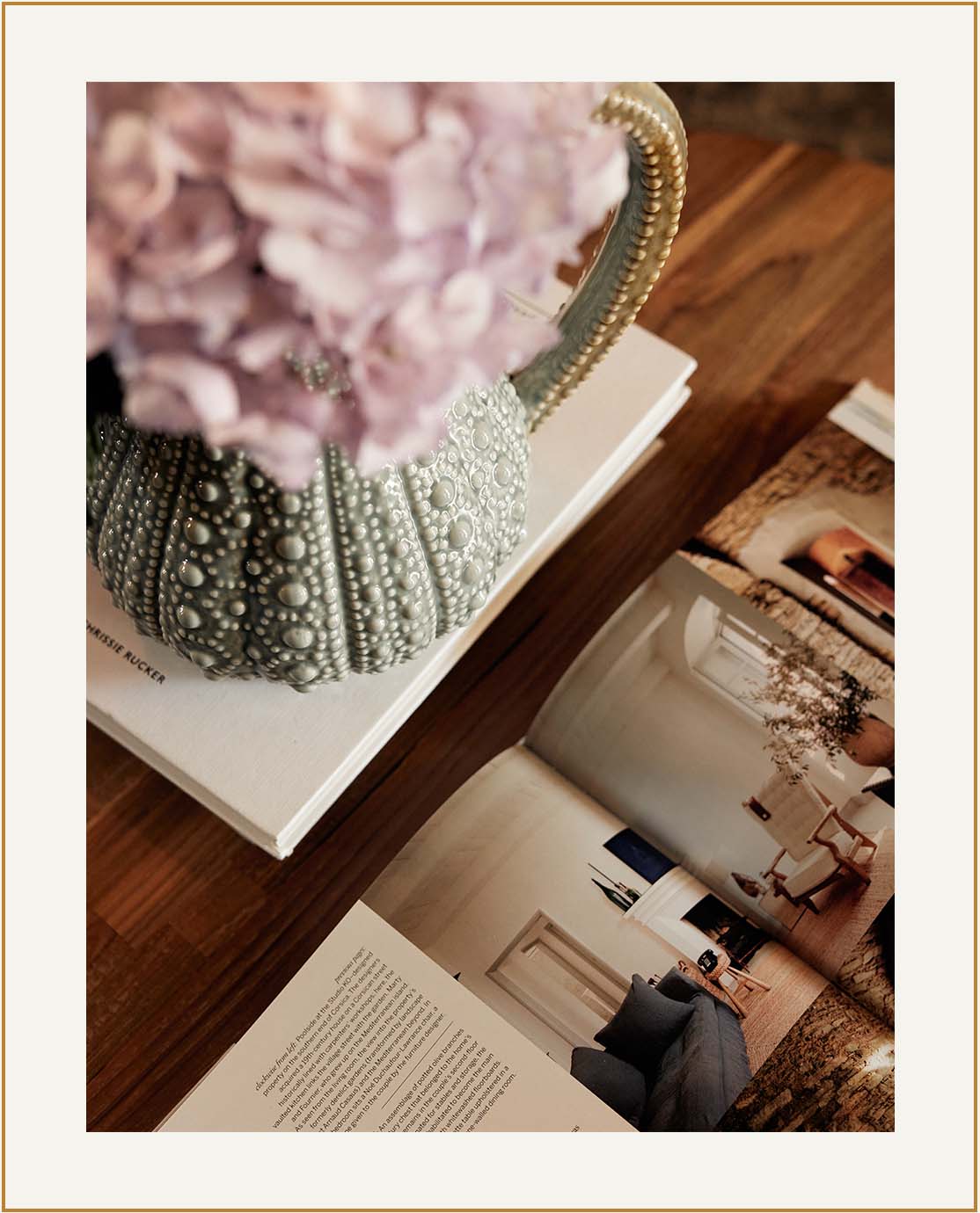 A close-up shot of a coffee table, with an open magazine, a safe green jug and pink flowers