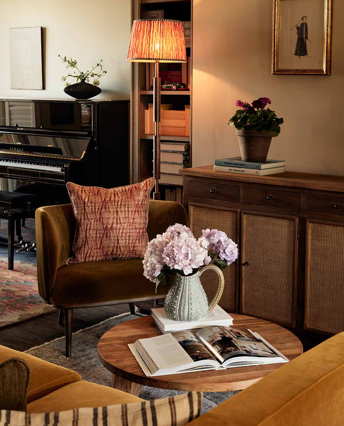 A sitting room setting with a velvet green armchair, red patterned cushion and wooden sideboard