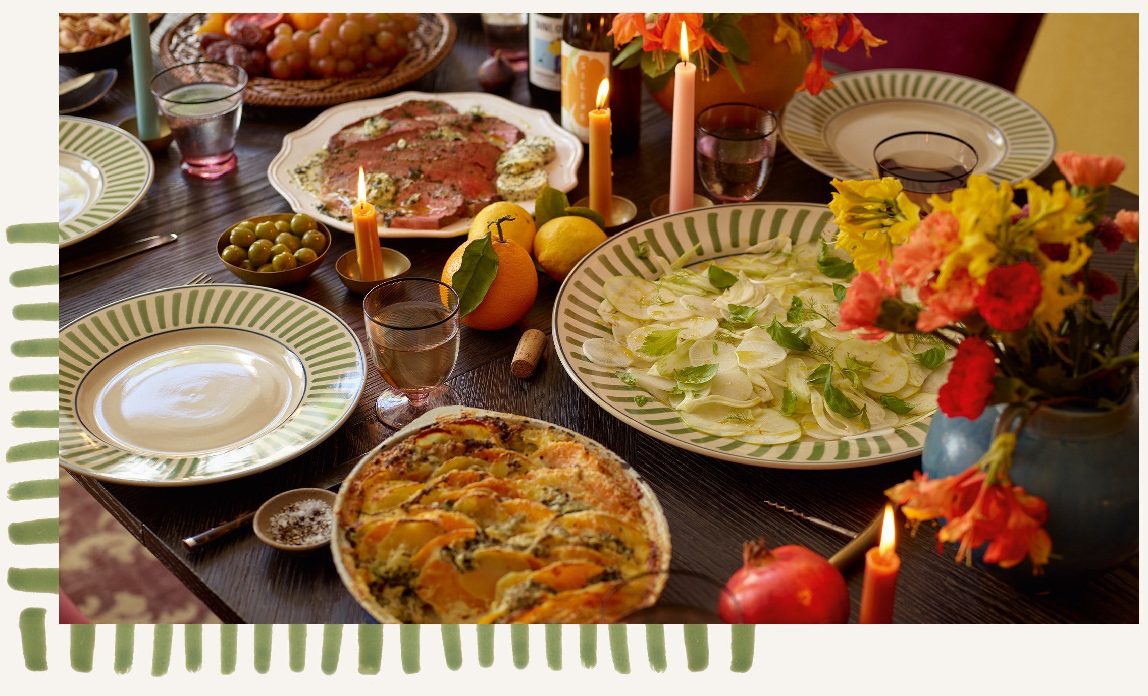 A dining table dressed with green striped crockery, serving an array of foods. The table is also decorated with lit candles and flowers.