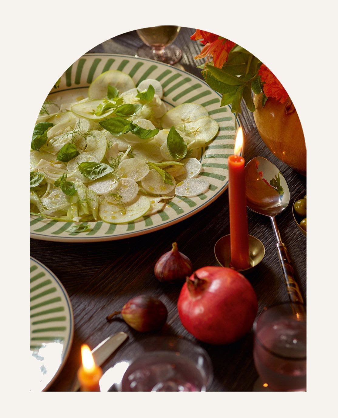 A salad served on a green striped plate surrounded by candles and dining table decorations.