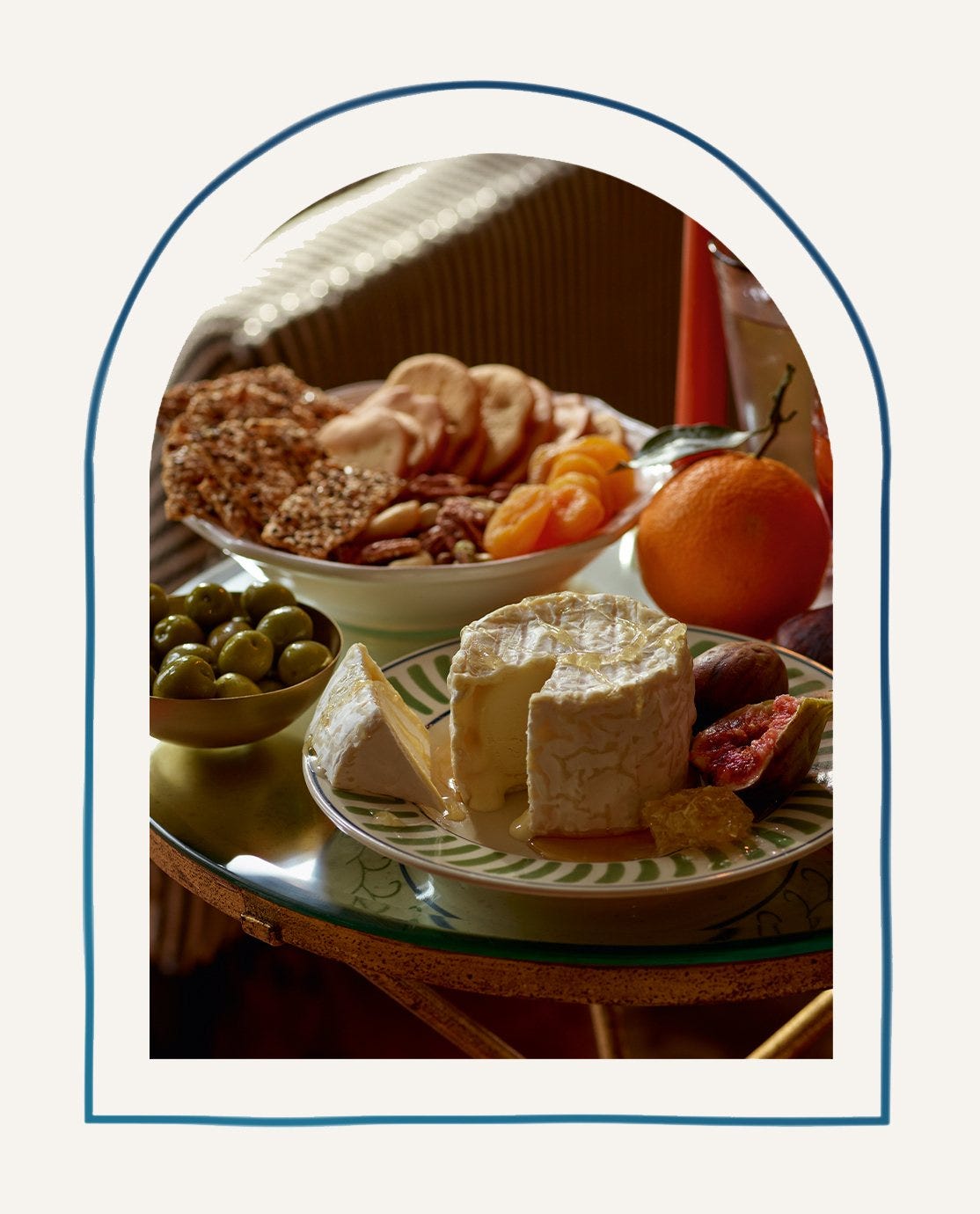 A glass table with a selection of food, from cheese to nibbles, in green striped crockery.