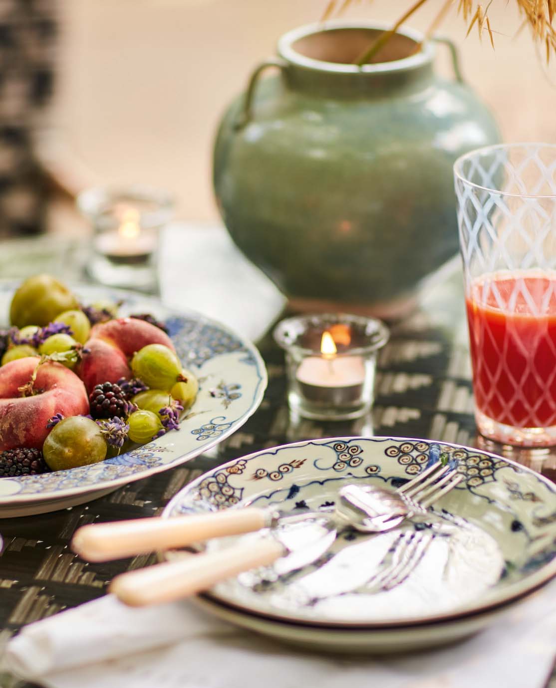 A tomato salad is served on a floral-print giant charger. Next to it are tealights, a blue pot, a printed glass and more floral plates.