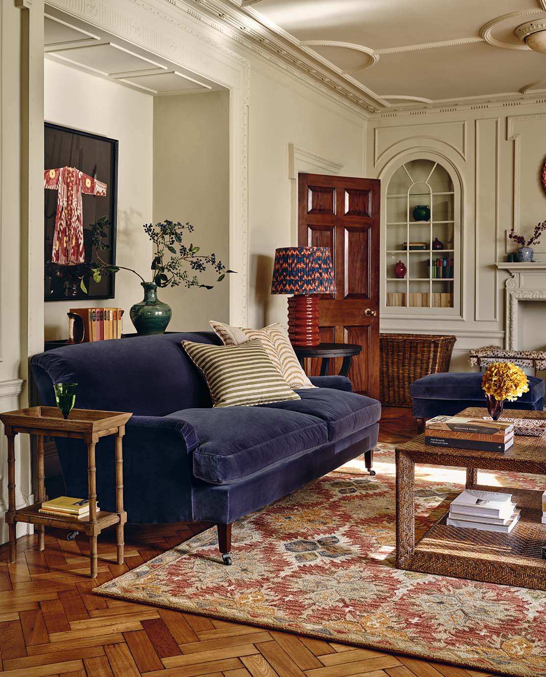 A country style sitting room with a blue velvet sofa, a woven rattan coffee table and a colorful patterned rug 