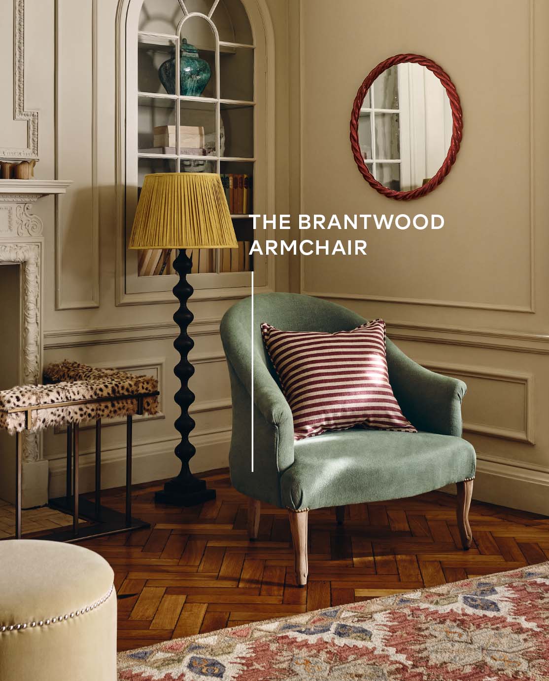 A green armchair in country style sitting room with a black floor lamp, yellow pleated lampshade and and glossy red mirror.